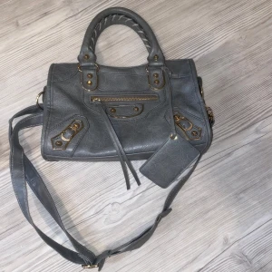 Grå axelväska med dragkedja - Snygg grå axelväska med  dekorativa detaljer och dragkedja. Väskan har både handtag och en justerbar axelrem för flexibel användning. .