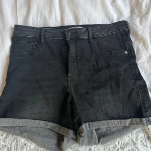 Svarta jeansshorts från Gina - Snygga svarta jeansshorts från Gina med klassisk femficksdesign. De har en bekväm passform och är perfekta för en avslappnad stil. Shortsen har uppvikta benslut för en trendig look. Det står stl 42 men skulle säga att de sitter som M