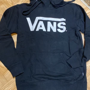 Svart hoodie från Vans - Säljer en svart hoodie från Vans med stor logga på framsidan. Tröjan har en klassisk känguruficka och justerbar huva med dragsko. Perfekt för en avslappnad stil.hoodien är i gott skick då den inte är mkt använd 