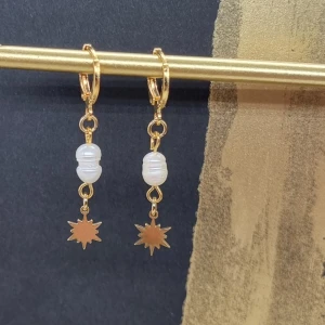 Guldörhängen med pärlor och stjärndetalj - Silver 925.Eleganta guldörhängen med vita pärlor och en hängande stjärndetalj. Perfekta för att ge en touch av glamour till din stil.