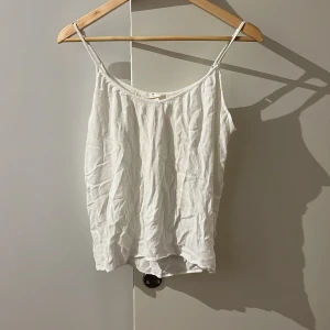 Vit linnetopp från H&M - Säljer en vit linnetopp från H&M med tunna axelband. Toppen har en enkel och luftig design, perfekt för varma dagar. Den är tillverkad i ett lätt material som ger en skön känsla mot huden.