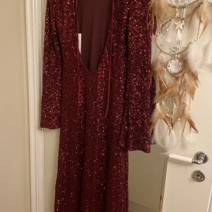 Vinröd paljettklänning - Säljer en fantastisk vinröd långklänning täckt av glittrande paljetter. Klänningen har långa ärmar och en elegant passform som passar perfekt för festliga tillfällen, tex alla hjärtans dag. Fin passform, snygg öppen rygg, och går ut vid ärmarna, super snygg.. tyvärr för liten för mig.. aldrig andvänd, bara testad.