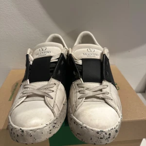 Valentino Garavani sneakers - Snygga Valentino Garavani sneakers i vitt med svarta detaljer. Skorna har en unik stänkmönstrad sula och klassisk snörning. Perfekta för en stilren look. Storlek 37. Pris kan diskuteras