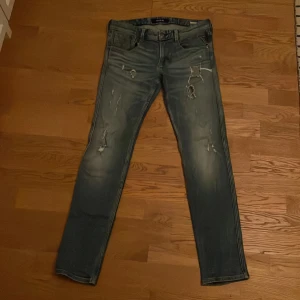 Blå jeans från Replay - Snygga blå jeans från Replay med slitna detaljer och en straight passform. De har en klassisk femficksdesign och knappgylf. Perfekta för en avslappnad stil.
