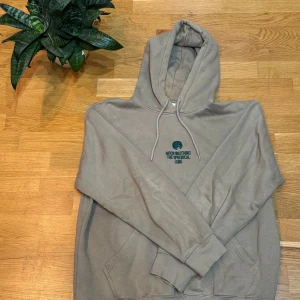 grön hoodie med tryck - Säljer en grön hoodie med ett coolt tryck på bröstet som säger 'Moon Watching The Spherical Lune'. Den har en klassisk känguruficka och justerbar huva med snören. Perfekt för en avslappnad stil.