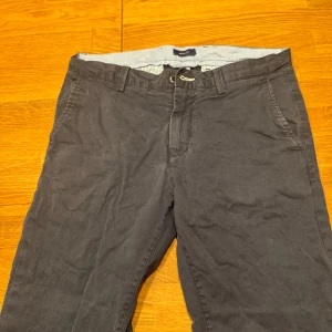 Grå byxor från Gant - Snygga grå byxor från Gant med normal passform. Byxorna har knappar och dragkedja framtill samt fickor både fram och bak. Perfekta för en stilren look.