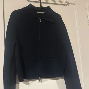 Mörkblå jacka från Åhléns - Snygg mörkblå jacka från Åhléns i storlek XS. Jackan har en dragkedja framtill och en klassisk krage. Perfekt för en stilren look.