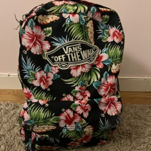 Blommig ryggsäck från Vans - Snygg ryggsäck från Vans med ett färgglatt blommönster på svart bakgrund. 