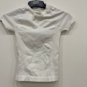 Vit ribbad topp från  - Säljer en stilren vit ribbad topp. Den har korta ärmar och en tight passform, perfekt för en enkel och snygg look. Toppen är gjord i ett mjukt material som känns skönt mot huden. På bilden ser det ut som den har sminkfläxk fast har tvättat den nu så den är alldeles klockren❣️❣️❣️