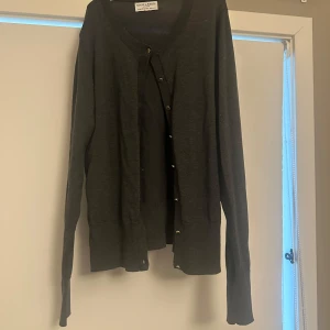 Svart/grå från Holly & Whyte - Säljer en stilren svart/grå kofta från Holly & Whyte by Lindex. Koftan har långa ärmar och guldiga knappar framtill. Perfekt för lager-på-lager under kyligare dagar. Super fin kofta som jag tyvärr säljer då jag inte får användning för den alls.