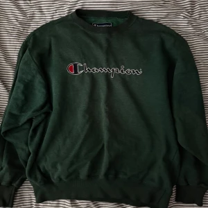 Grön sweatshirt från Champion💸 - Säljer en snygg grön sweatshirt från Champion med deras ikoniska logga broderad på framsidan. Tröjan har en klassisk rund hals och långa ärmar, perfekt för en avslappnad stil. Väldigt skönt och exklusivt material. Premium känsla!💸