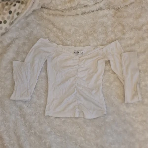 Vit offshoulder topp från Hollister - Säljer en vit offshoulder topp från Hollister i storlek XS. Toppen har långa ärmar och en ribbad struktur med en snygg rynkad detalj framtill. Perfekt för en stilren look.