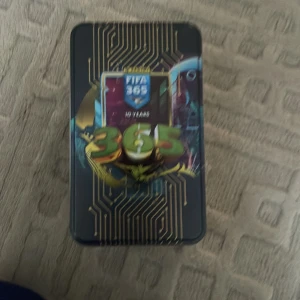 FIFA 365 samlarkort i metallåda - Säljer en samling FIFA 365 samlarkort från Panini, korten inuti har ett värde på 1500+ och förvarade i en snygg metallåda. Lådan har en futuristisk design med guld- och svartfärger och FIFA 365-loggan. Perfekt för fotbollsfans och samlare!