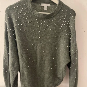 Grå/grön tröja med pärlor från H&M - Snygg grå tröja från H&M med pärlor över hela framsidan. Tröjan har långa ärmar och en rund halsringning.