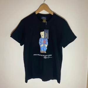 Ny! Ralph Lauren T-shirt - FÖRSTA TILL 420kr ELLER BÄSTA ERBJUDANDET INNAN LÖRDAG VINNER! ✅•	Svart Ralph Lauren T-shirt 	•	Storlek: M 	•	Klassisk design med broderad logotyp och björnmotiv på framsidan 	•	Ny och aldrig använd! 	•	Perfekt skick!