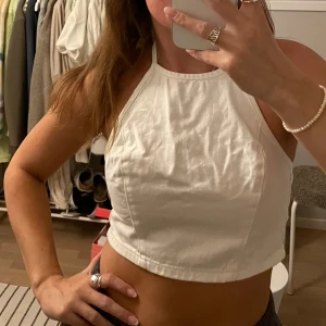 Vit halterneck topp i jeanstyg - Vit croppad halterneck-topp med knytning i nacken. Den är i denim-tyg och sitter jättesnyggt! Aldrig använd 