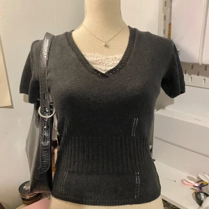 Vintage mörkgrå stickad topp från Mexx - Säljer en stilren mörkgrå tröja från Mexx med v-ringning och korta ärmar. Tröjan har ribbade detaljer och en elegant spetskant vid halsen. Perfekt för en chic och bekväm look.