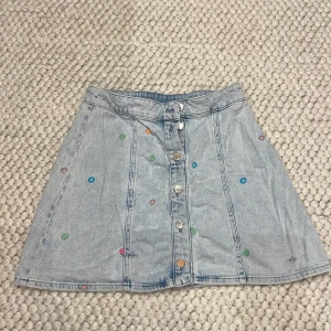 Jeanskjol med blommönster från Crās - Säljer en söt jeanskjol från Crās med färgglada  broderade blommor. Storlek 36.