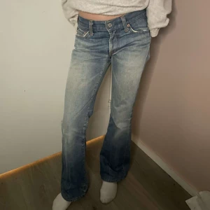 Blå bootcut jeans - Snygga blå bootcut jeans med låg midja och klassisk femficksdesign. Jeansen har en lätt tvättad look och stängs med dragkedja och knapp. Perfekta för en avslappnad stil.