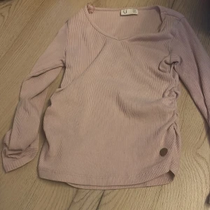 Rosa ribbad tröja från Ü - Säljer en söt rosa ribbad tröja från Ü i storlek 134/140. Tröjan har långa ärmar och en snygg rynkad detalj på sidan. Perfekt för en stilren och bekväm look.