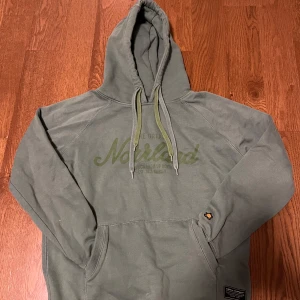 Grön hoodie från SQRTN Company - Säljer en grön Norrlands hoodie från SQRTN Company med tryck på bröstet. Den har en justerbar huva och en praktisk magficka. Ny i skick, lite små smutsig men det försvinner i tvätten på noll tid. Har storleken XXS men är väldigt stor i storleken och går även för XS/S