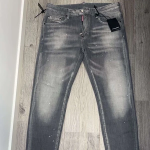 Grå jeans från Dsquared2 - Snygga grå jeans från Dsquared2 med en cool, sliten look och vita färgstänk. De har en klassisk femficksdesign och en röd etikett med texten 'Caten Heated' baktill. Perfekta för en trendig och avslappnad stil. Helt nya.