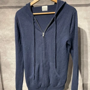Kashmir hoodie John Henric - Säljer en stilren mörkblå hoodie från John Henric i 100% kashmir. Tröjan har dragkedja och huva med snörning, samt praktiska fickor framtill. Perfekt för kyliga dagar.