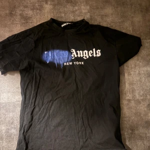 Svart t-shirt från Palm Angels - Snygg svart t-shirt från Palm Angels med texten 'New York' och en blå färgdetalj på bröstet.  Skickas inom 1-2 dagar