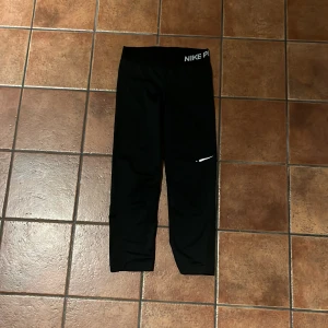 Svarta tights från Nike Pro - Säljer ett par svarta Nike Pro tights i storlek XS. Perfekta för träning med Dri-FIT-teknologi som håller dig torr och bekväm. Tightsen har en elastisk midja. Loggan på benet är lite sliten.