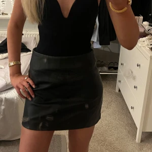 Svart kortkjol i skinn - Snygg svart kortkjol i skinn med en stilren design. Perfekt för en trendig look. Kjolen har en tight passform som framhäver figuren.