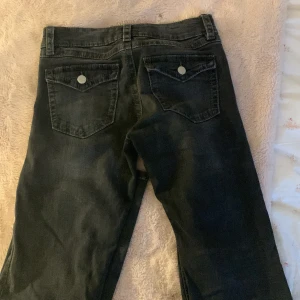 Svarta jeans med fickdetaljer - Snygga svarta jeans med klassisk femficksdesign och dekorativa knappar på bakfickorna. Perfekta för en avslappnad stil. Vanliga från Gina❤️