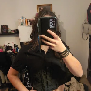 Svart croppad skjorta - Snygg svart croppad skjorta med korta ärmar. Perfekt för en trendig look. Skjortan har en klassisk krage och knappar framtill.