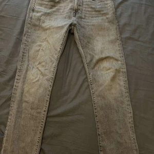 Grå jeans från Dressmann - Snygga grå jeans från Dressmann i slim fit. De har en klassisk femficksdesign med dragkedja och knapp framtill. Perfekta för en stilren look.