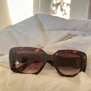 Solglasögon med sköldpaddsmönster - Snygga solglasögon med ett trendigt sköldpaddsmönster. De har en fyrkantig form och mörka linser som ger ett stilrent intryck. Perfekta för att ge din outfit en extra touch.