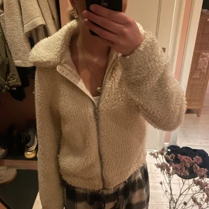 Beige teddyjacka med dragkedja - Mysig beige teddyjacka med dragkedja framtill. Jackan har långa ärmar och en bekväm passform. Perfekt för höst och vinter!