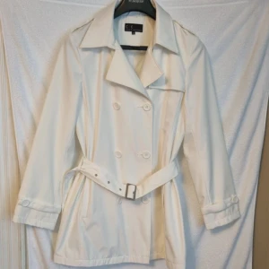 Trenchcoat - Vit trenchcoat i storlek 40, använd fåtal gånger fint skick. Längd från axel ner är ca 81 cm.
