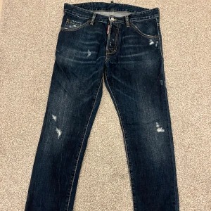 Mörkblå jeans från DSQ2 - Säljer ett par snygga mörkblå jeans DSQ2 liknande med slitna detaljer för en cool look. De har en klassisk femficksdesign och knappgylf. Perfekta för både vardag och fest! 🕺