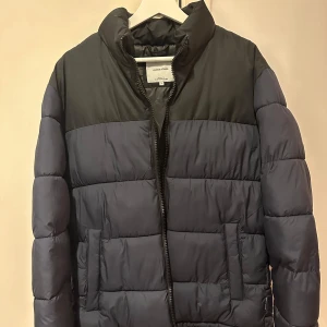 Jacka - Jack & Jones - Marinblå blockfärgad pufferjacka med ståkrage. Storlek L  Jackan är i nytt skick och oanvänd