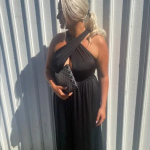 Svart klänning - Elegant svart långklänning med korsade axelband som går att justera. Perfekt för festliga tillfällen. Använd en gång på bal. Klänningen har en smickrande passform och är tillverkad i ett mjukt material som faller fint. Skriv vid intresse, tar Swish.