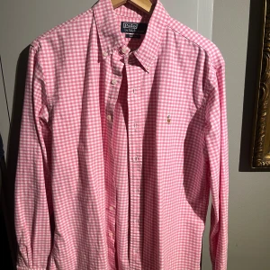Rosa rutig skjorta från Polo Ralph Lauren - Säljer en snygg rosa rutig skjorta från Polo Ralph Lauren i mycket bra skick. Skjortan är långärmad och har klassiska knappar framtill. Perfekt för både vardag och festliga tillfällen. Passar bra till både jeans och chinos!