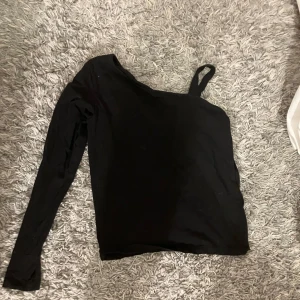 Svart oneshoulder topp från H&M - Säljer en snygg svart oneshoulder topp från H&M. Perfekt för festliga tillfällen med sin unika design och bekväma passform. Toppen har en lång ärm och är gjord i ett mjukt material. Passar perfekt till både jeans och kjol! I stl 158-164. 