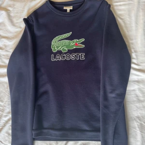 Mörkblå tröja från Lacoste - Säljer en snygg mörkblå tröja från Lacoste med det klassiska krokodilmärket på bröstet. Tröjan är i bomull och polyester, vilket gör den både bekväm och hållbar. Den är i storlek 164 men passar som en xs/s😊
