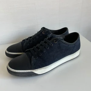 Lanvin cap toe  - Säljer ett par svarta sneakers i jeansmaterial med snörning. De har en vit sula och svart tåhätta som ger en cool kontrast. Perfekta för vardagsbruk och passar till det mesta i garderoben. Skorna är i bra skick och redo för nya äventyr! Även väldigt unika.