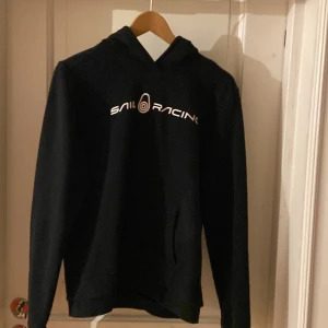 Svart hoodie från Sail Racing - Säljer en svart hoodie från Sail Racing i mycket bra skick. Den har en klassisk design med logotypen tryckt på framsidan. Perfekt för både vardag och träning. Den är bekväm och stilren, ett måste i garderoben! 🖤