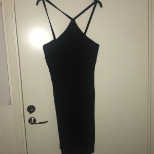 Svart klänning med smala axelband - Snygg svart klänning i storlek XL med smala axelband som korsas i ryggen. Perfekt för en utekväll eller fest! Klänningen har en tight passform och är i ett mjukt material som känns skönt mot huden.