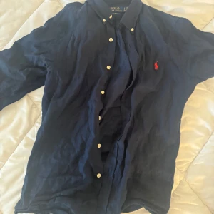 Mörkblå skjorta från Ralph Lauren - Säljer en snygg mörkblå skjorta från Ralph Lauren i slim fit. Skjortan har långa ärmar och klassiska knappar framtill. Den är perfekt för både vardag och fest. Den ikoniska röda loggan på bröstet ger en stilren touch. Passar bra till både jeans och chinos! Nypris 1800, köpt i augusti 