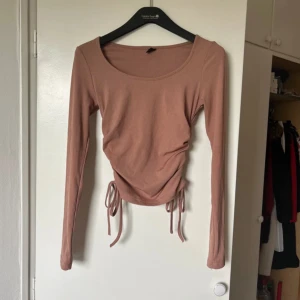 Beige långärmad topp med knyt - Säljer en superfin beige långärmad topp med knyt i sidorna. Perfekt för både vardag och fest! Toppen har en åtsittande passform och är gjord i ett mjukt material som känns skönt mot huden. Den har en rund halsringning och är i mycket bra skick.