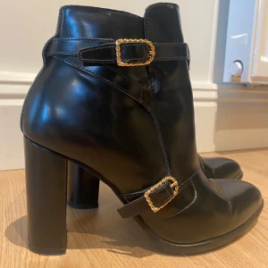 Svarta boots från Gigi Hadid X Tommy Hilfiger - Snygga svarta boots i skinn med gulddetaljer och dragkedja. De har en hög klack och stilrena spännen som ger en elegant touch. Perfekta för höst och vinter, både till vardags och fest. Använda en gång!