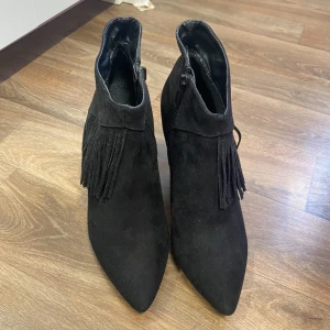 Svarta boots med fransar - Snygga svarta boots  med fransdetaljer och spetsig tå. De har en dragkedja på sidan för enkel på- och avtagning. Perfekta för höst och vinter, och ger en cool touch till vilken outfit som helst. Klacken ger lite extra höjd och stil.