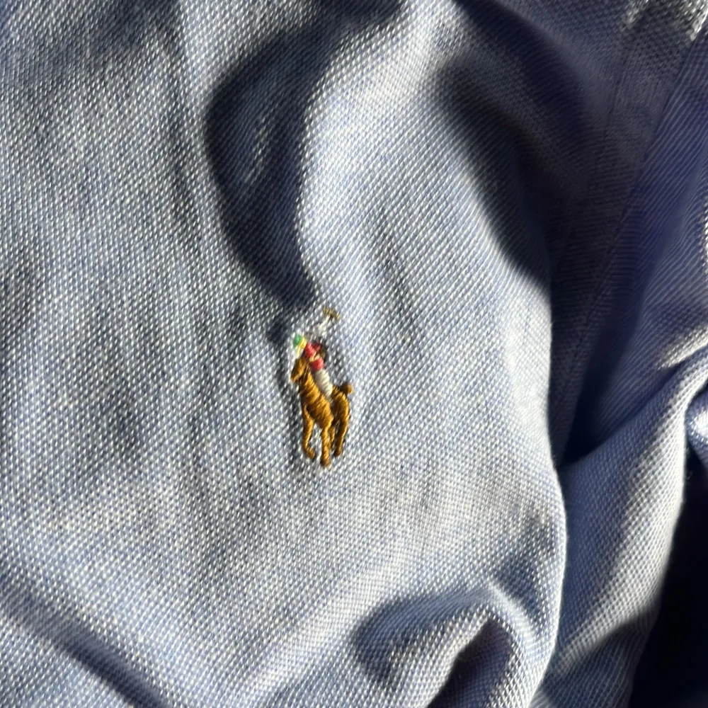 Säljer en snygg blå kortärmad skjorta från Ralph Lauren i bra skick. Skjortan har en klassisk krage och knappar framtill. Den är broderad med det ikoniska Polo-logotypen på bröstet. Perfekt för sommardagar eller avslappnade tillfällen. Passar ungefär till alla byxor.. Skjortor.